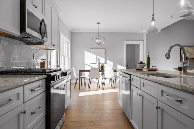 kitchen with a sink, appliances with stainless steel finishes, pendant lighting, and light stone counters