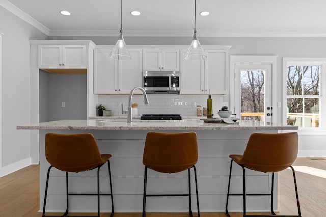 kitchen with stainless steel microwave, ornamental molding, a kitchen island with sink, white cabinets, and light wood-type flooring