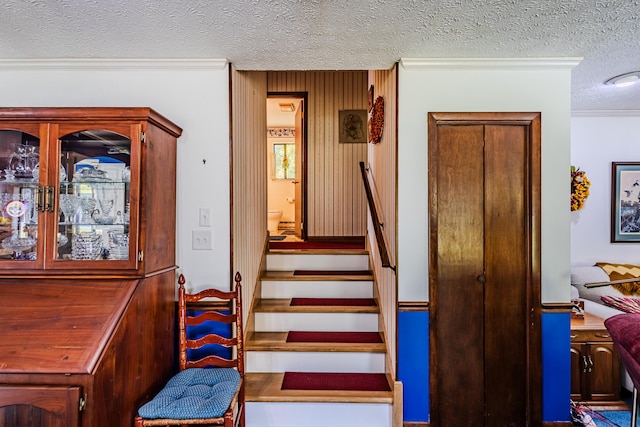 staircase featuring wood walls, a textured ceiling, and ornamental molding