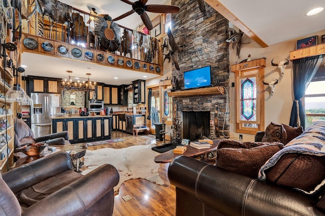 living room with a towering ceiling, ceiling fan with notable chandelier, wood-type flooring, beam ceiling, and a stone fireplace