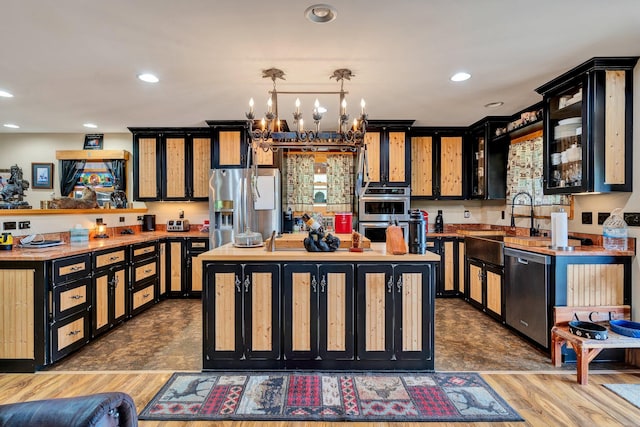 kitchen with hanging light fixtures, an inviting chandelier, appliances with stainless steel finishes, a kitchen island, and hardwood / wood-style flooring