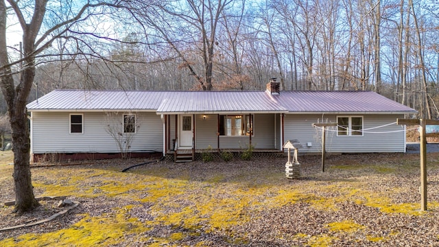 view of front facade with crawl space, covered porch, metal roof, and a chimney