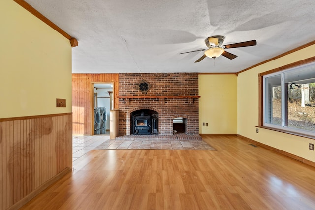 unfurnished living room with wooden walls, light wood-style flooring, ornamental molding, a wood stove, and a textured ceiling