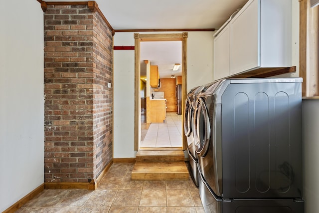 laundry area featuring light tile patterned floors, brick wall, baseboards, independent washer and dryer, and cabinet space