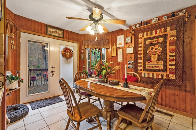 dining area featuring ceiling fan, wood walls, light tile patterned flooring, and french doors