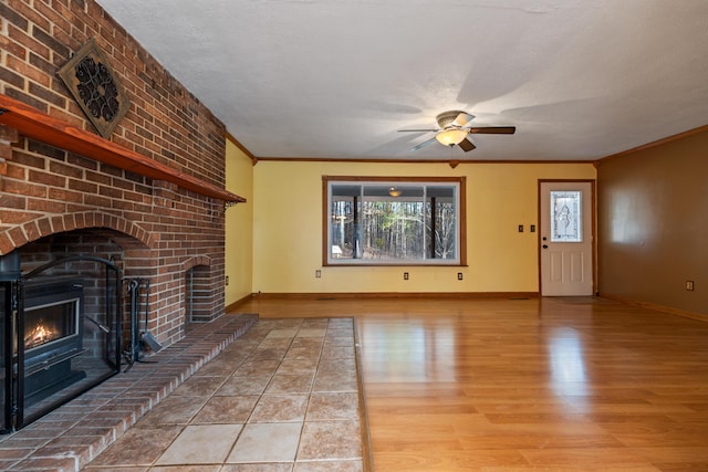 unfurnished living room featuring crown molding, a fireplace, light wood-style flooring, ceiling fan, and baseboards