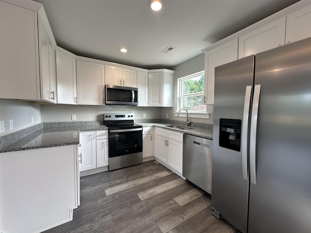 kitchen with sink, stainless steel appliances, white cabinets, dark hardwood / wood-style flooring, and dark stone counters