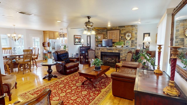 living room with ceiling fan with notable chandelier, a fireplace, and light hardwood / wood-style floors