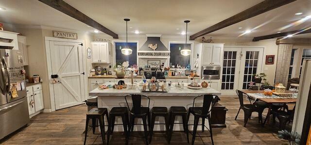 kitchen with hanging light fixtures, stainless steel fridge, beam ceiling, a kitchen bar, and white cabinetry