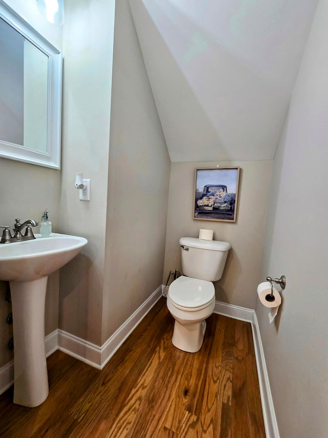 bathroom with toilet, hardwood / wood-style floors, vaulted ceiling, and sink