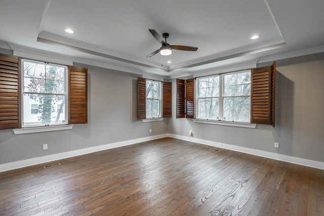 unfurnished room with ceiling fan, a tray ceiling, dark hardwood / wood-style flooring, and a wealth of natural light