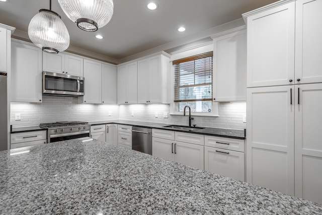 kitchen with sink, hanging light fixtures, appliances with stainless steel finishes, dark stone counters, and white cabinets