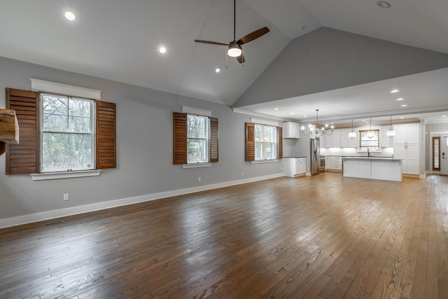 unfurnished living room featuring high vaulted ceiling, wood-type flooring, sink, and ceiling fan with notable chandelier