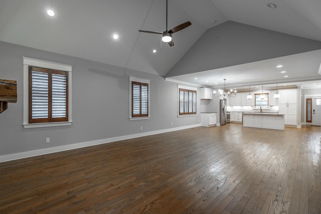 unfurnished living room featuring dark wood-type flooring, high vaulted ceiling, sink, and ceiling fan with notable chandelier