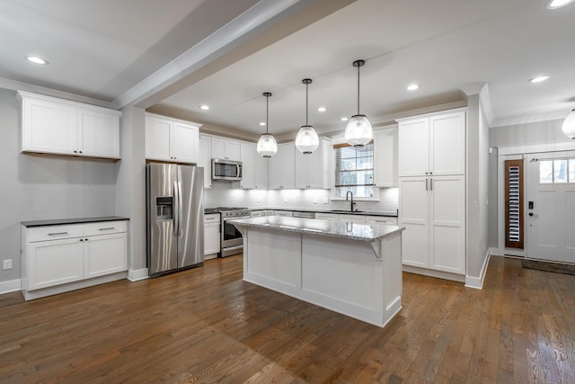 kitchen with stainless steel appliances, light stone counters, white cabinets, a kitchen island, and decorative light fixtures