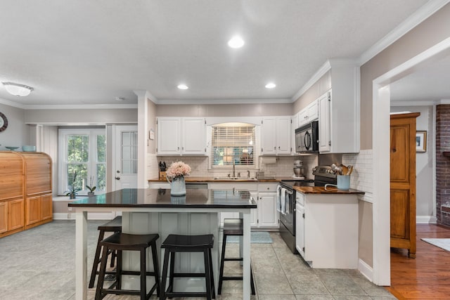 kitchen with black appliances, white cabinets, sink, ornamental molding, and a breakfast bar area