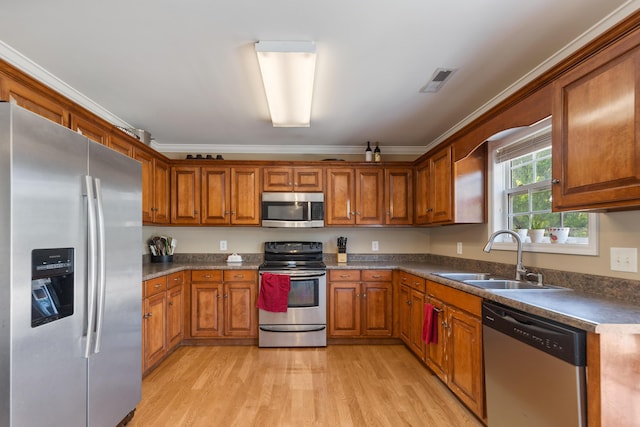 kitchen featuring appliances with stainless steel finishes, brown cabinets, crown molding, and a sink