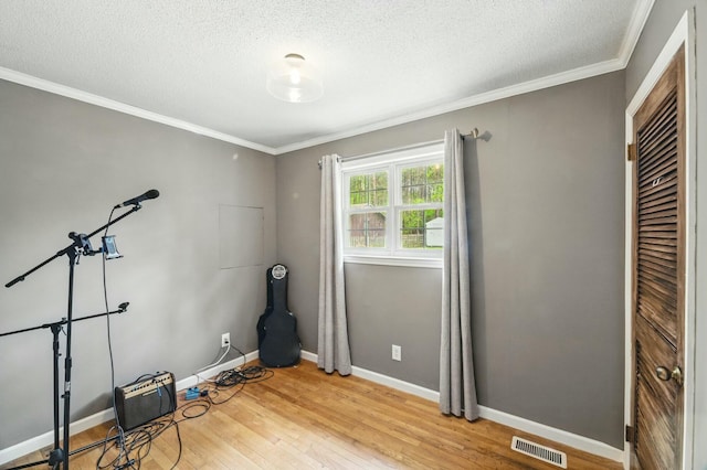 workout area featuring ornamental molding, visible vents, wood finished floors, and a textured ceiling