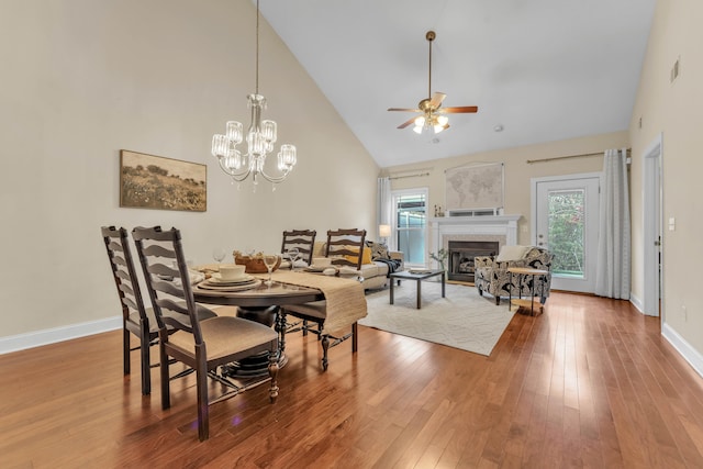 dining area with hardwood / wood-style flooring, ceiling fan with notable chandelier, and high vaulted ceiling