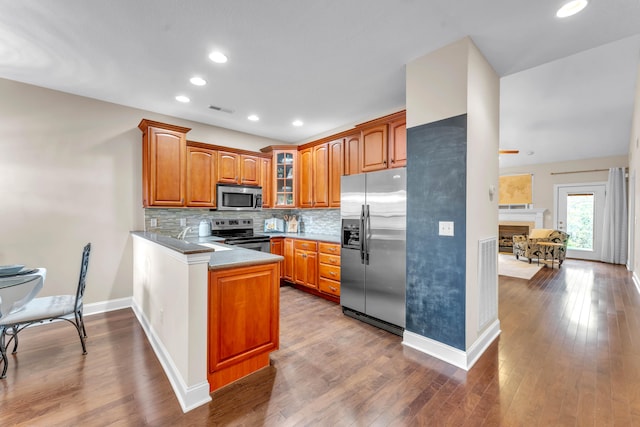 kitchen featuring sink, stainless steel appliances, backsplash, kitchen peninsula, and hardwood / wood-style floors