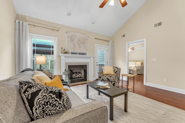 living room featuring high vaulted ceiling, ceiling fan, a tile fireplace, and light hardwood / wood-style flooring