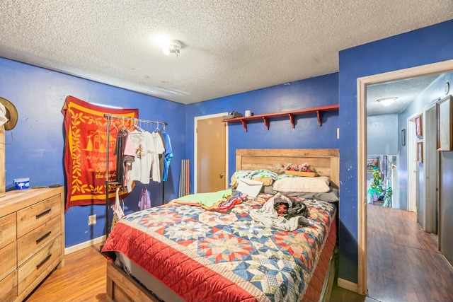 bedroom with a textured ceiling, baseboards, and wood finished floors