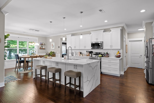 kitchen with appliances with stainless steel finishes, white cabinetry, pendant lighting, and an island with sink