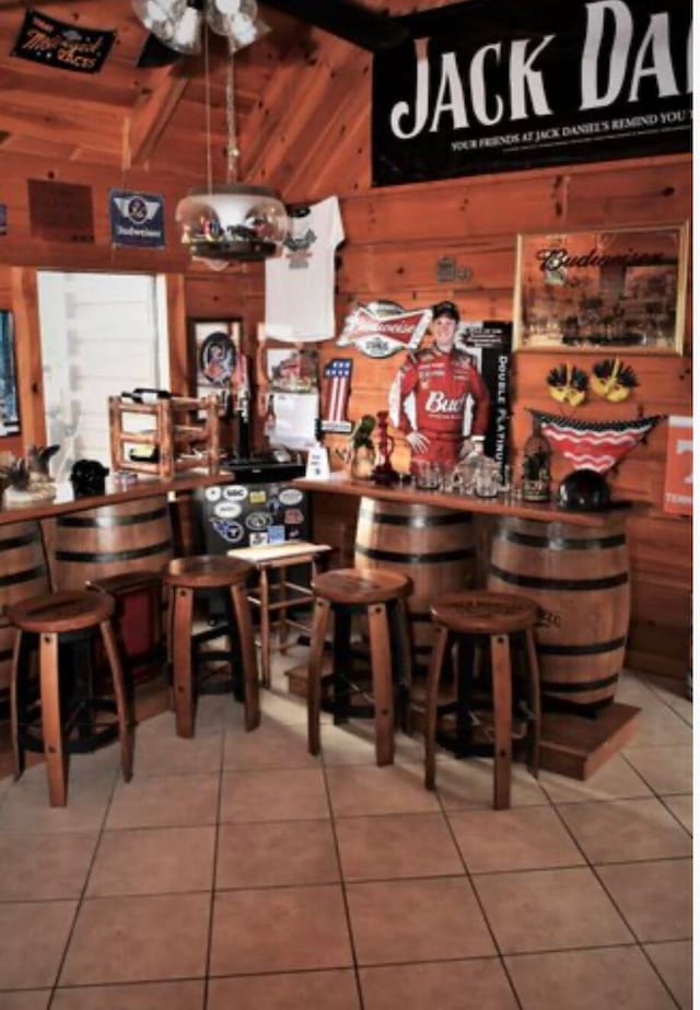 bar with light tile patterned floors, wooden walls, and beam ceiling