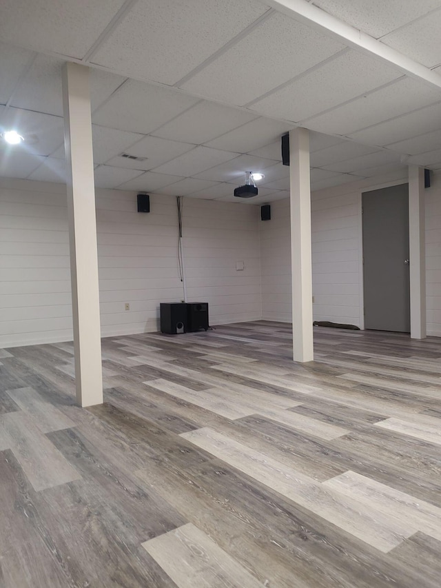 basement featuring hardwood / wood-style flooring, a drop ceiling, and wooden walls