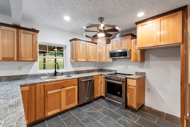 kitchen with stone counters, ceiling fan, sink, stainless steel appliances, and a textured ceiling