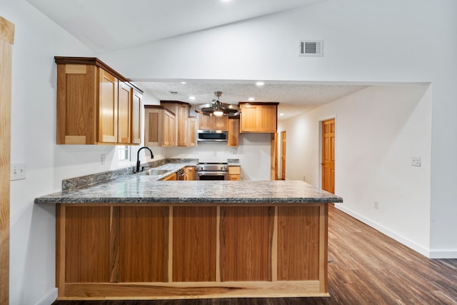 kitchen featuring sink, vaulted ceiling, dark hardwood / wood-style floors, kitchen peninsula, and stainless steel appliances