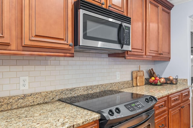 kitchen featuring light stone counters, brown cabinetry, decorative backsplash, electric range oven, and stainless steel microwave