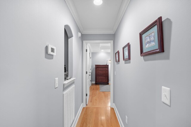 hallway featuring visible vents, ornamental molding, arched walkways, light wood-style floors, and baseboards