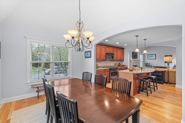 dining room with light wood-style flooring, arched walkways, baseboards, recessed lighting, and a chandelier
