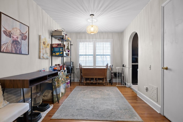 home office featuring baseboards, arched walkways, and wood finished floors