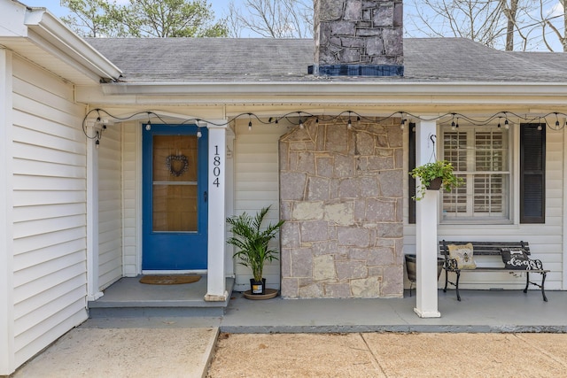 entrance to property with a chimney and a shingled roof