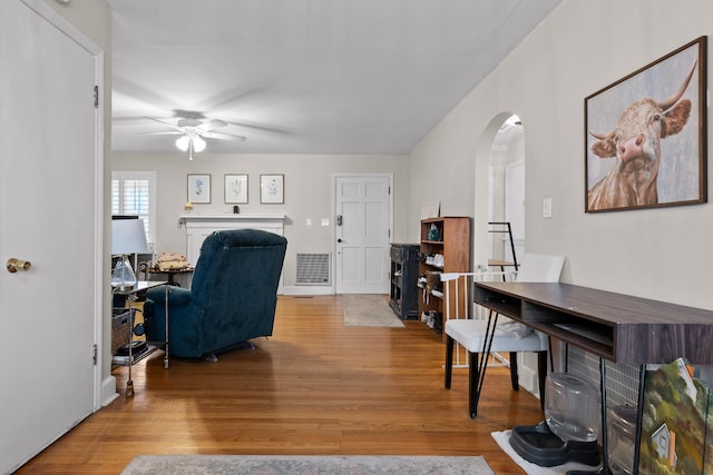 living area featuring a ceiling fan, visible vents, wood finished floors, and arched walkways