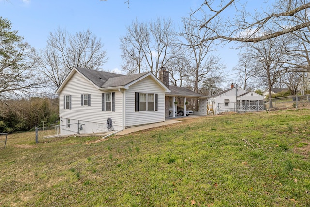 rear view of house with a carport, a yard, fence, and a chimney