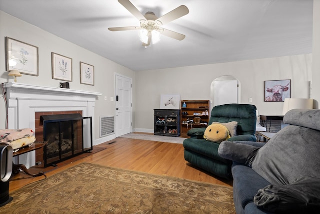 living room featuring a ceiling fan, wood finished floors, visible vents, a fireplace, and arched walkways