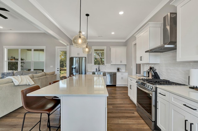 kitchen with appliances with stainless steel finishes, wall chimney range hood, white cabinets, dark hardwood / wood-style floors, and a kitchen island