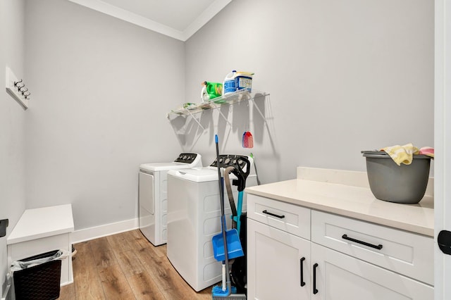 clothes washing area featuring crown molding, cabinets, washer and clothes dryer, and light hardwood / wood-style floors