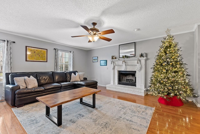 living room featuring ornamental molding, a textured ceiling, ceiling fan, hardwood / wood-style flooring, and a fireplace