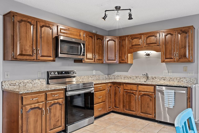 kitchen featuring appliances with stainless steel finishes, light stone counters, a textured ceiling, sink, and light tile patterned floors