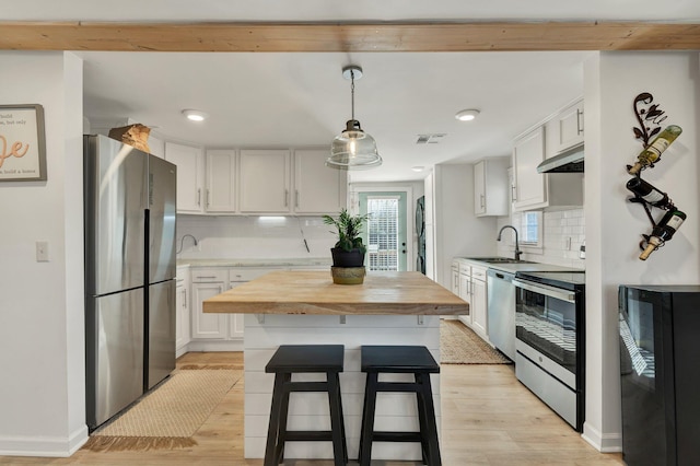 kitchen with decorative backsplash, appliances with stainless steel finishes, white cabinetry, and pendant lighting