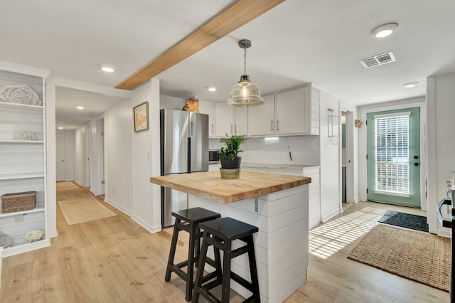 kitchen with wooden counters, pendant lighting, a kitchen bar, stainless steel refrigerator, and white cabinets