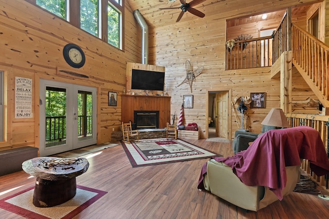 living area with a glass covered fireplace, wood finished floors, ceiling fan, a high ceiling, and wooden walls