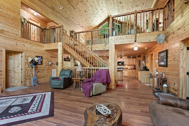 living area with stairway, high vaulted ceiling, wood walls, and wood finished floors