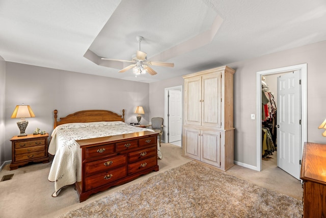 carpeted bedroom featuring ceiling fan, a walk in closet, a closet, and a raised ceiling