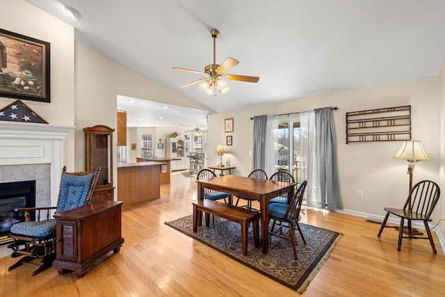 dining room with light hardwood / wood-style floors, a tile fireplace, lofted ceiling, and ceiling fan