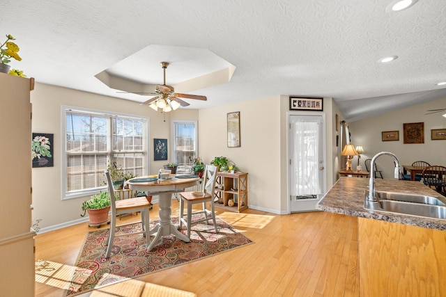 dining area with light wood-type flooring, ceiling fan, a raised ceiling, and sink